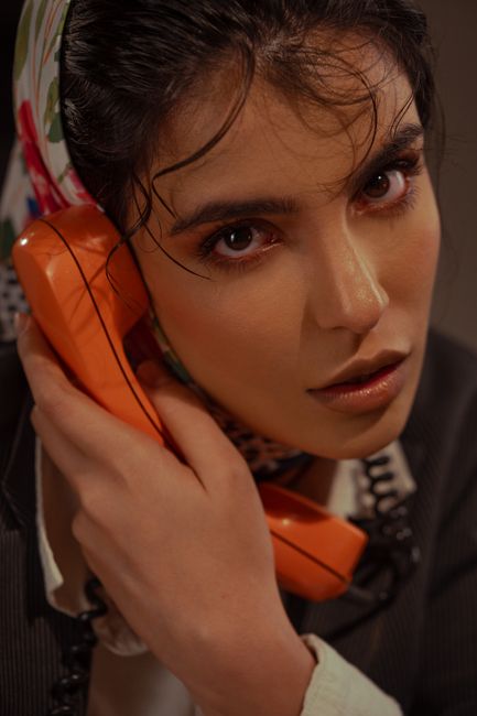 Close-up portrait of a woman with a vintage orange telephone, capturing a classic, moody vibe.
