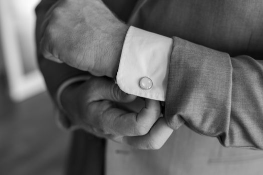 Black and white close-up of a man adjusting cufflinks on a suit, showcasing elegance. — photo by Michael Morse