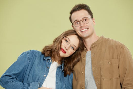 A smiling couple wearing stylish eyeglasses, embracing on a light background.