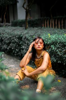 一位戴着墨镜的亚洲女人身穿黄色服装，坐在户外，看上去若有所思