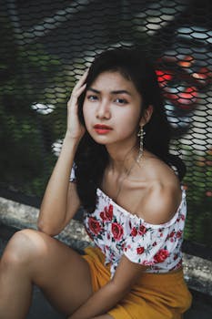 Elegant woman in floral top poses outdoors with a thoughtful expression.