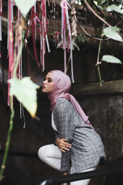 A fashionable woman poses outdoors in a chic hijab and modern outfit.