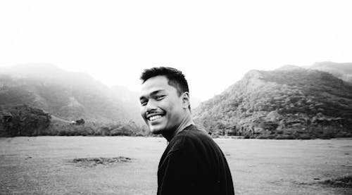 Black and white happy Asian male with toothy smile standing in valley and resting in nature