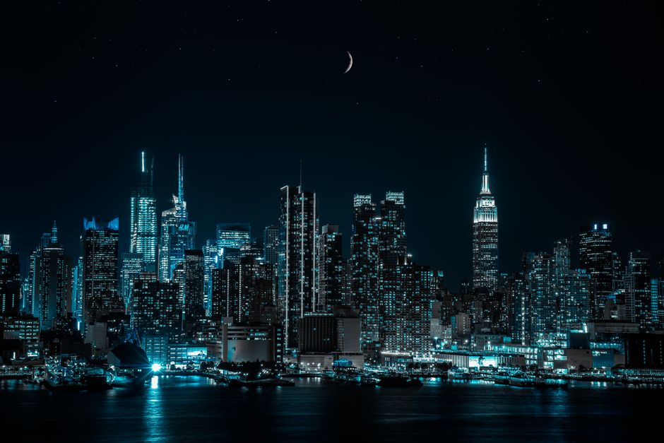 A breathtaking view of a city skyline at night under a crescent moon, showcasing illuminated skyscrapers and tranquil waterfront.