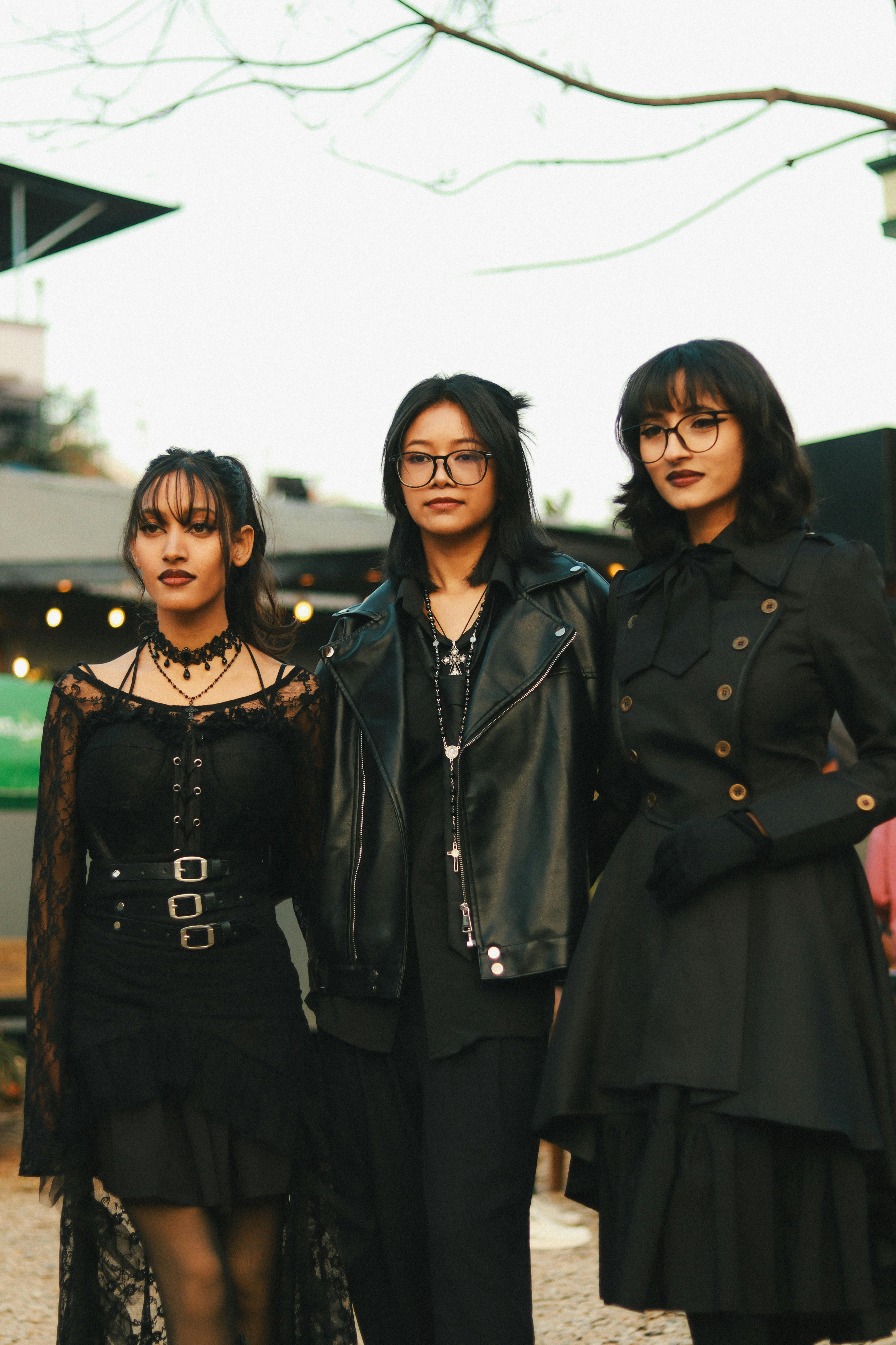 Three women in gothic fashion posing together outdoors during the day.