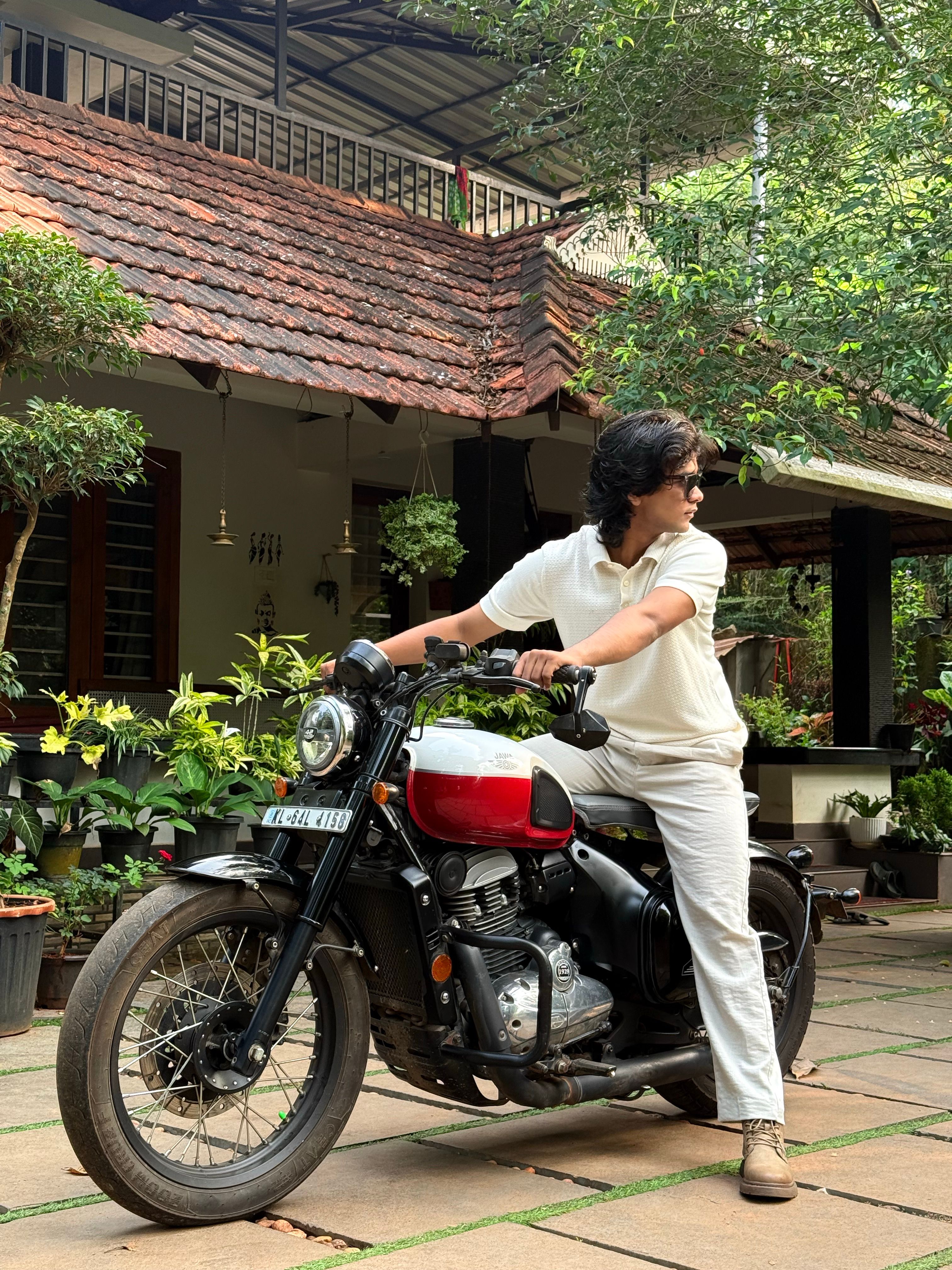 Man on a red and black motorcycle in a lush garden setting, exuding a casual vibe.