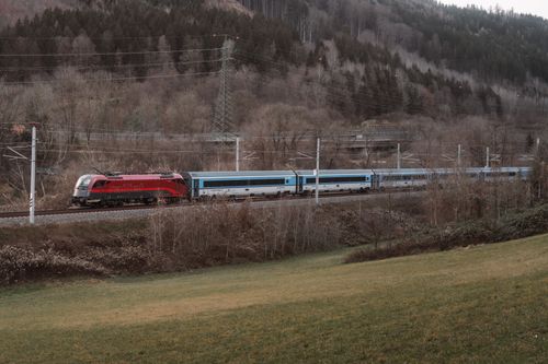 Free A picturesque red train travels through serene forest landscape, perfect for travel enthusiasts. Stock Photo