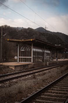 A peaceful train station surrounded by mountains during a cloudy day.