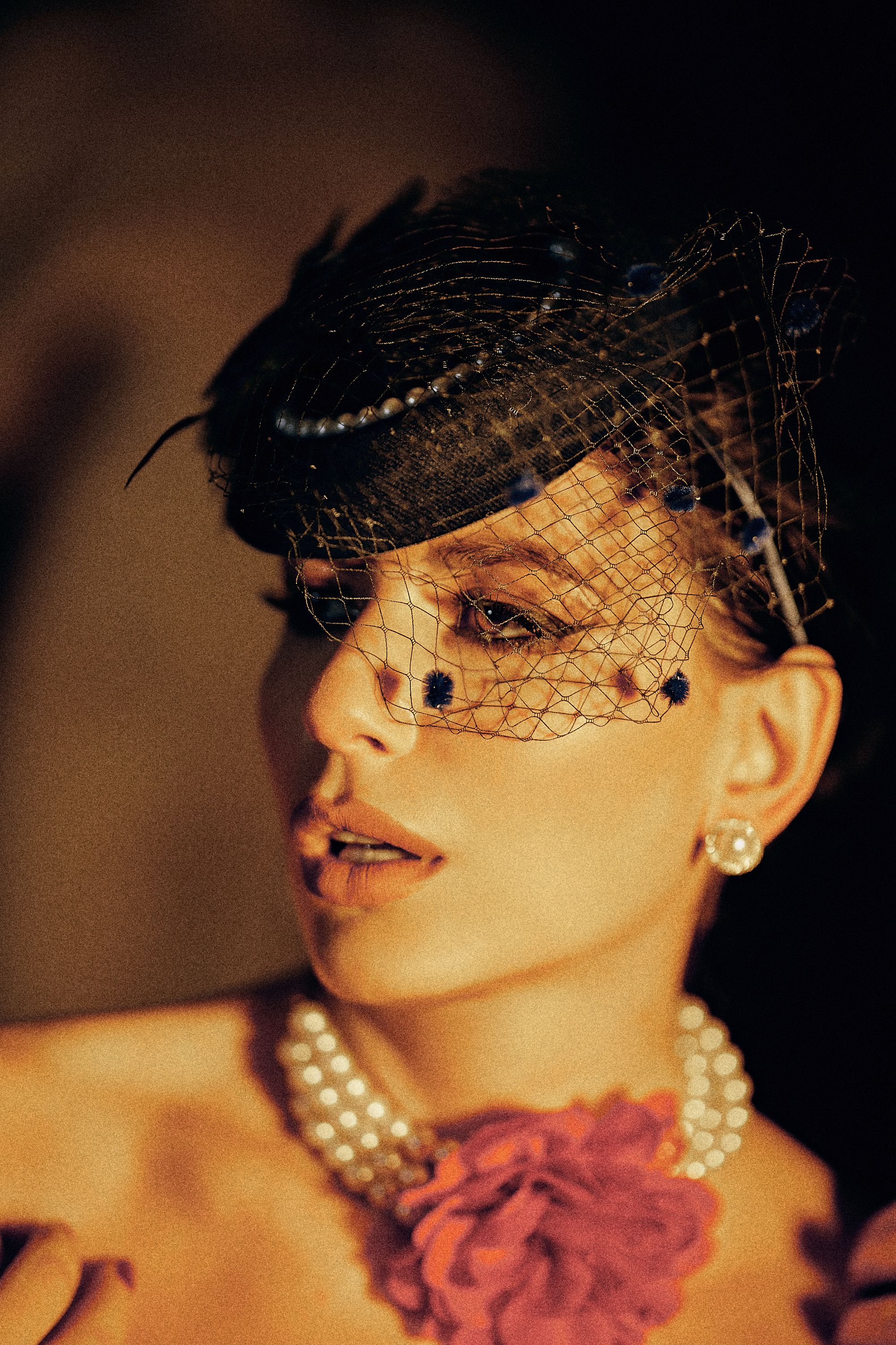Stylish woman in vintage hat with pearls, dramatic lighting.
