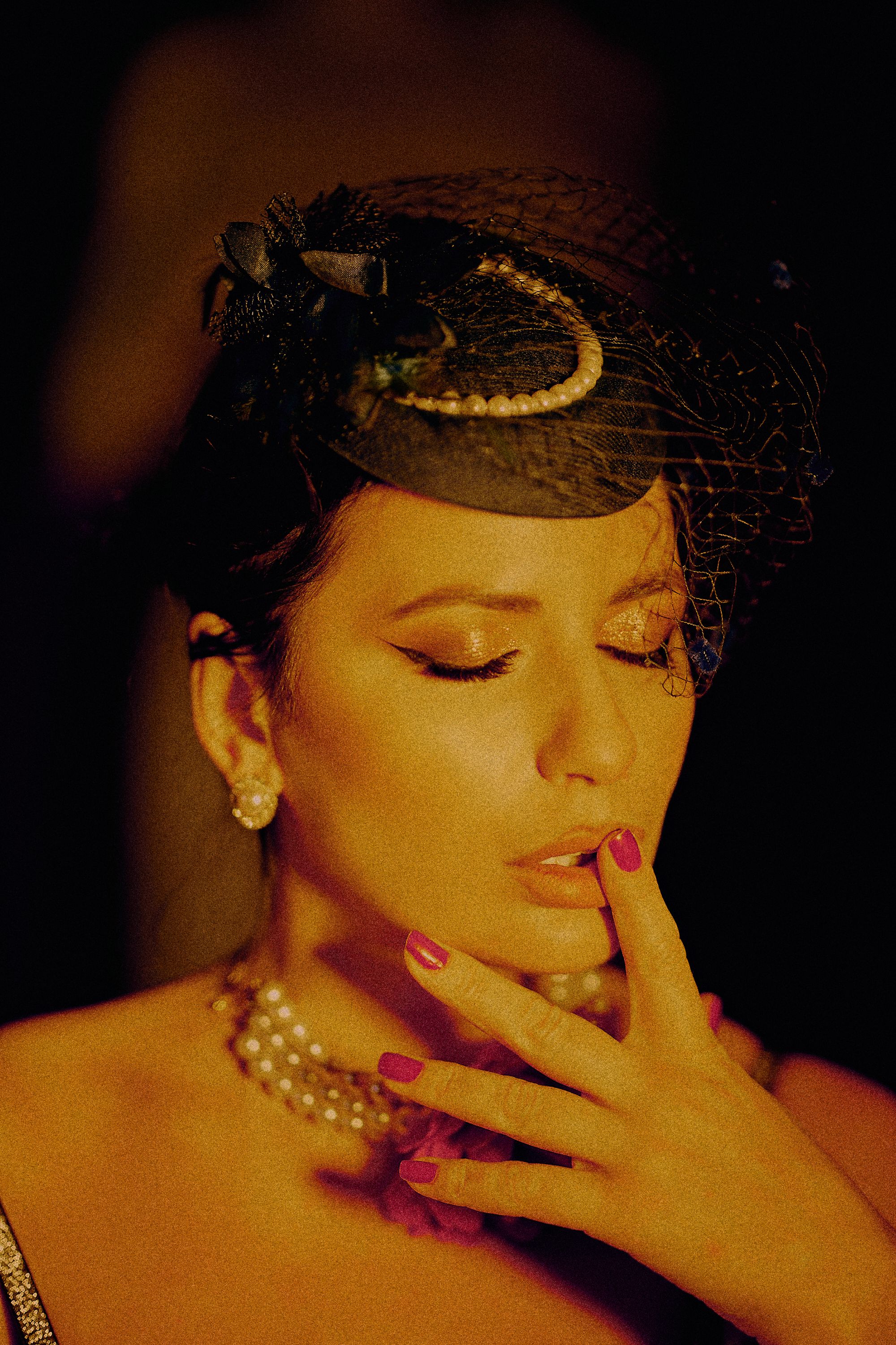 A woman in vintage attire and pearls posing elegantly indoors.