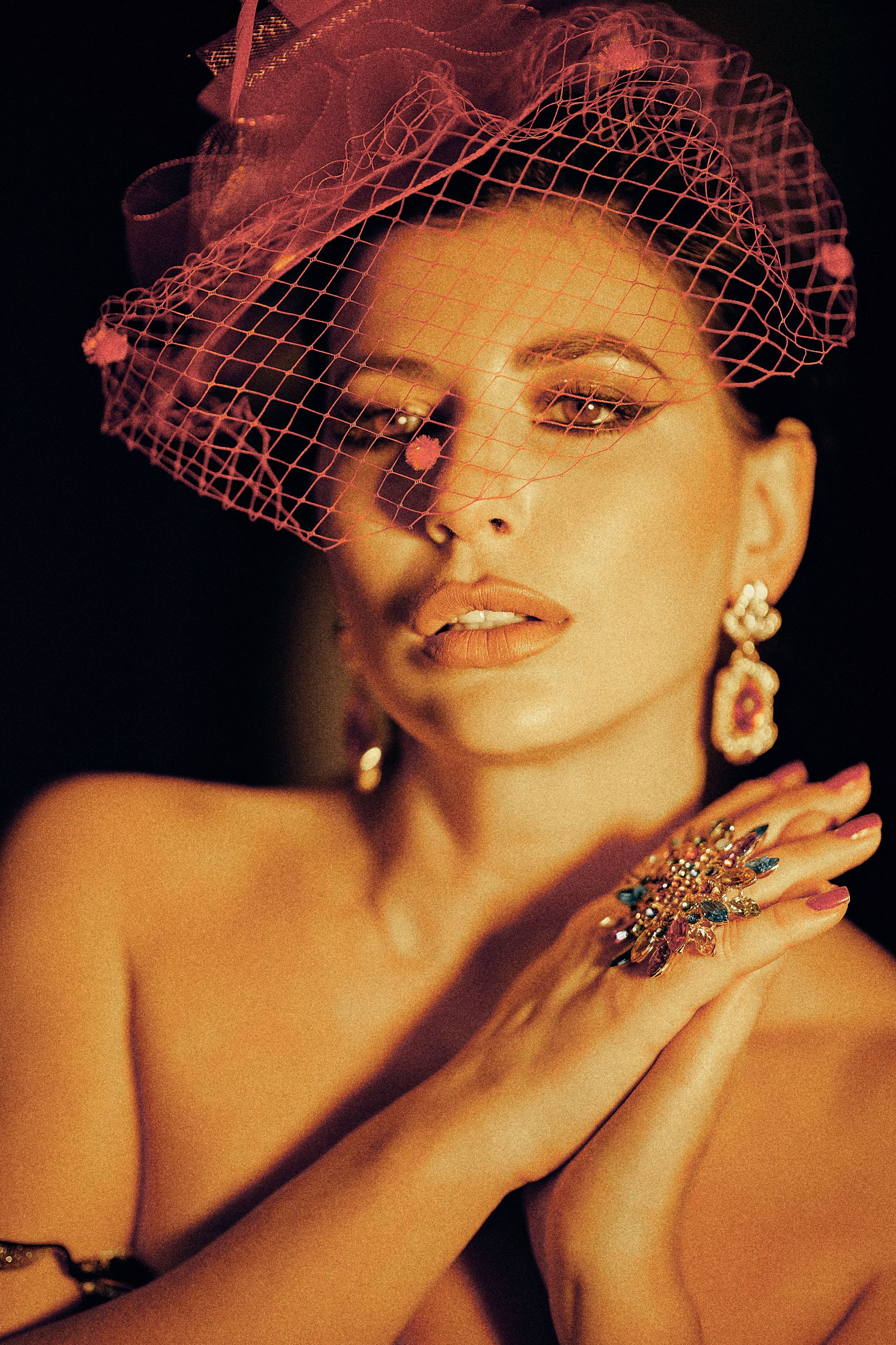 Glamorous portrait of a woman wearing a pink vintage hat with dramatic lighting.