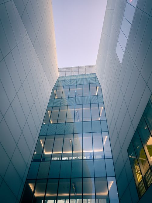 Free A striking shot of a modern glass building facade captured from below, with reflections at sunrise. Stock Photo