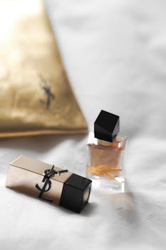 Elegant flat lay of perfume and lipstick on soft white fabric.