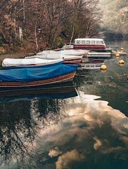 Tranquil scene of moored wooden boats on a calm lake reflecting clouds.