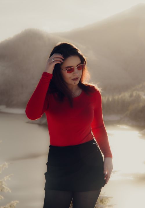 Free Stylish woman in red top and sunglasses poses by a lake with mountains in Cluj-Napoca, Romania. Stock Photo