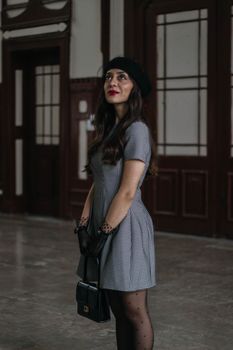 Stylish woman in retro dress with beret indoors, embodying vintage fashion.