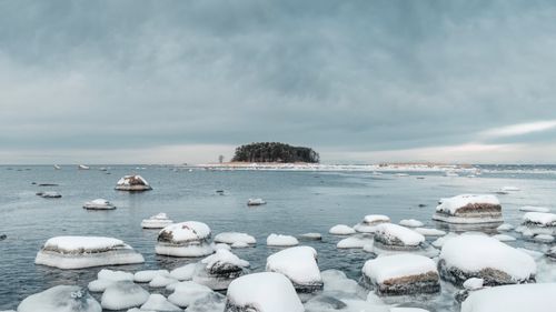 Free Snow-covered rocks by a calm winter sea under a cloudy sky. Stock Photo