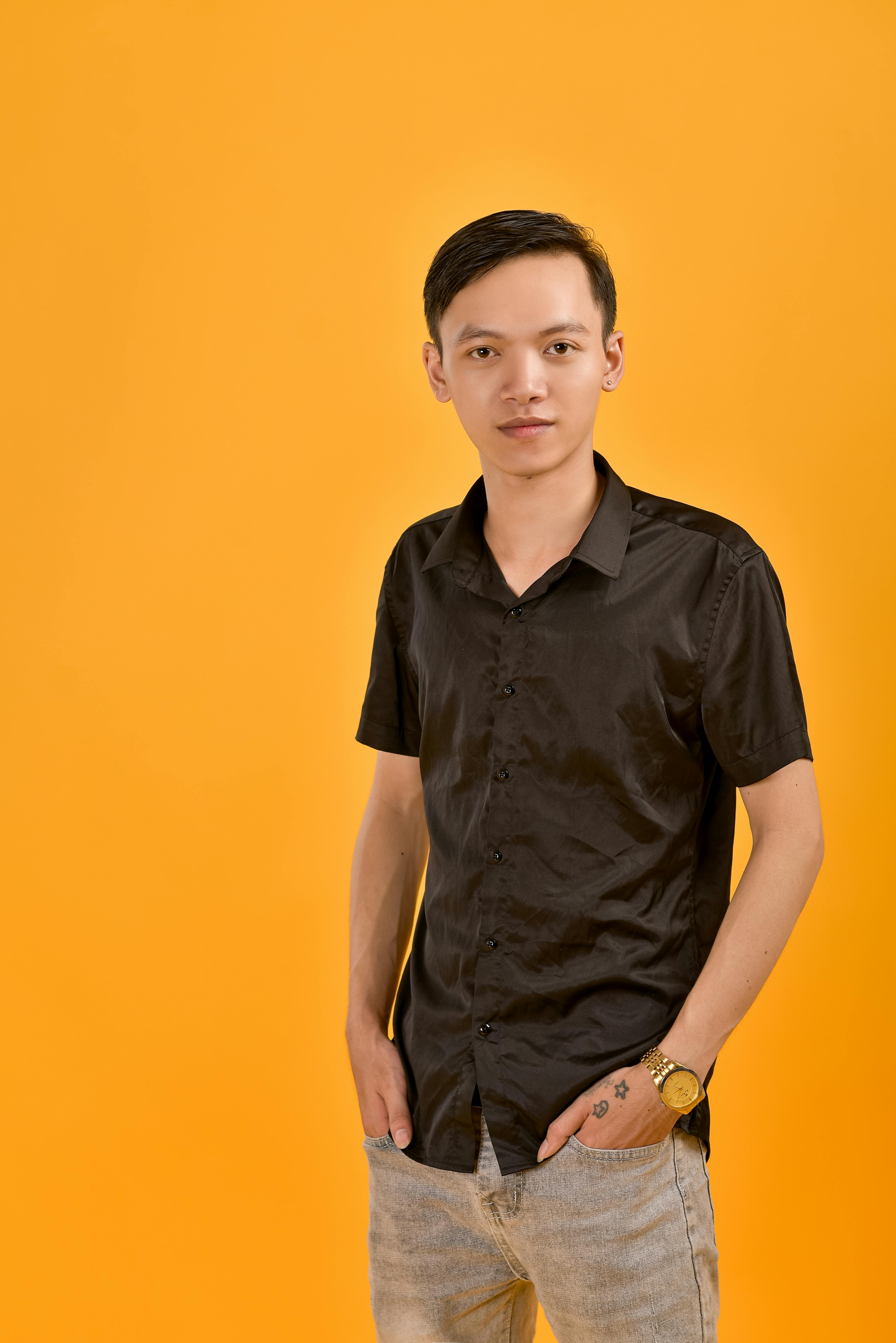 無料 黄色の背景に黒いシャツとジーンズを着た若い男性のカジュアルなポートレート。 写真素材