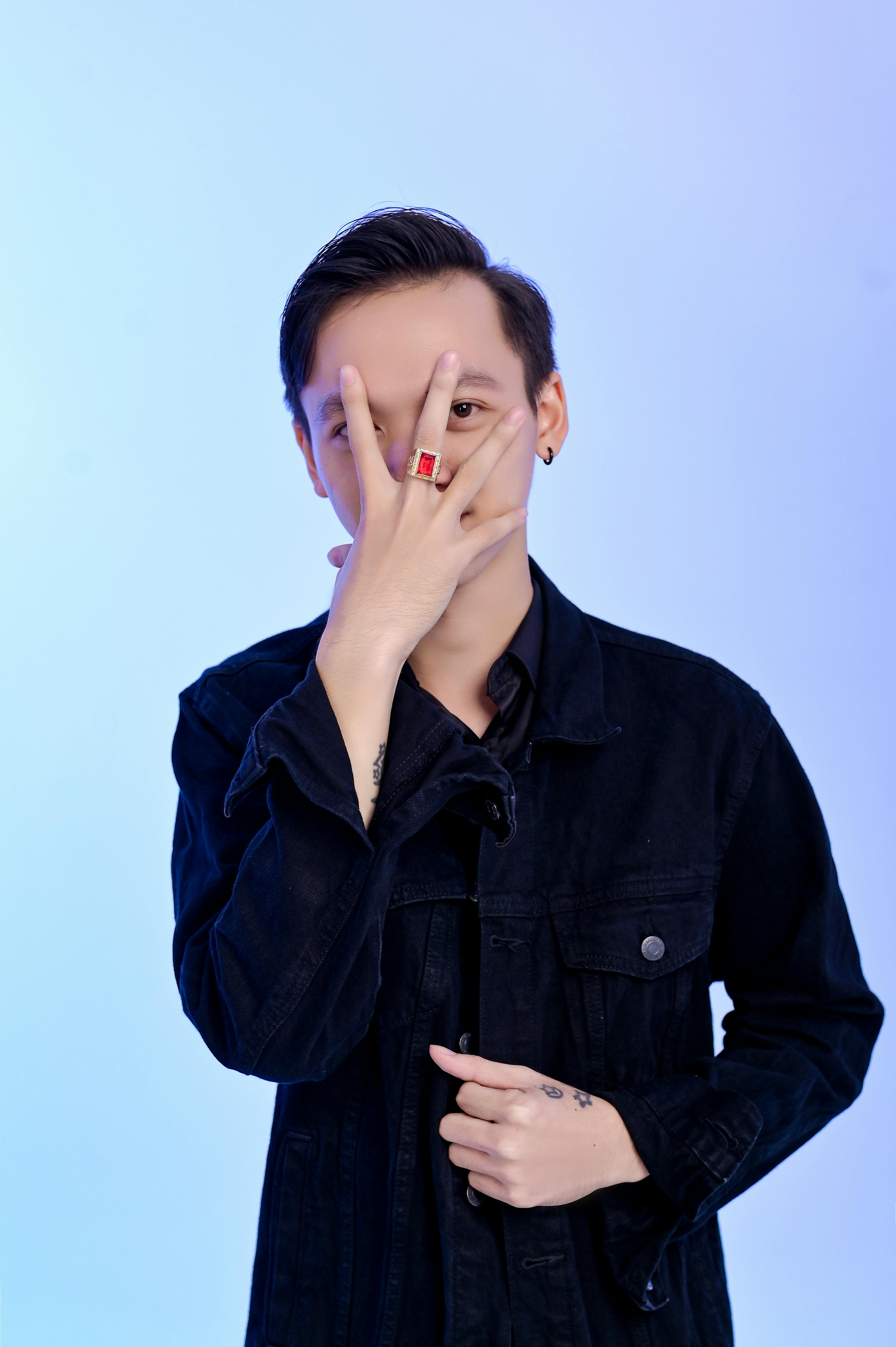 Portrait of young adult male in denim jacket covering face with hand
