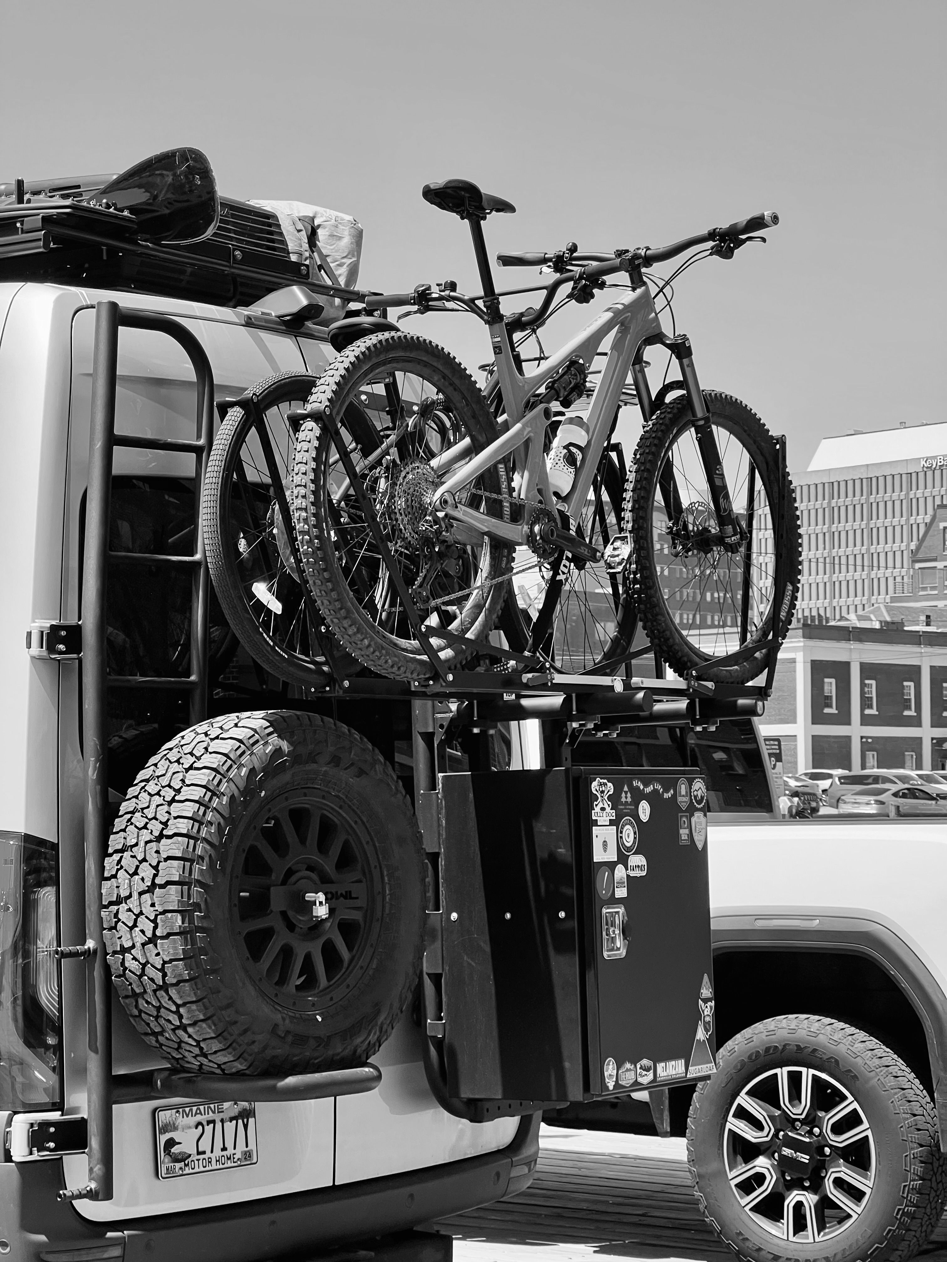 Monochrome image of bicycles mounted on a vehicle rack in urban setting.