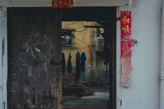 A rustic courtyard with weathered walls and hanging laundry, framed by a worn wooden door adorned with red scrolls.