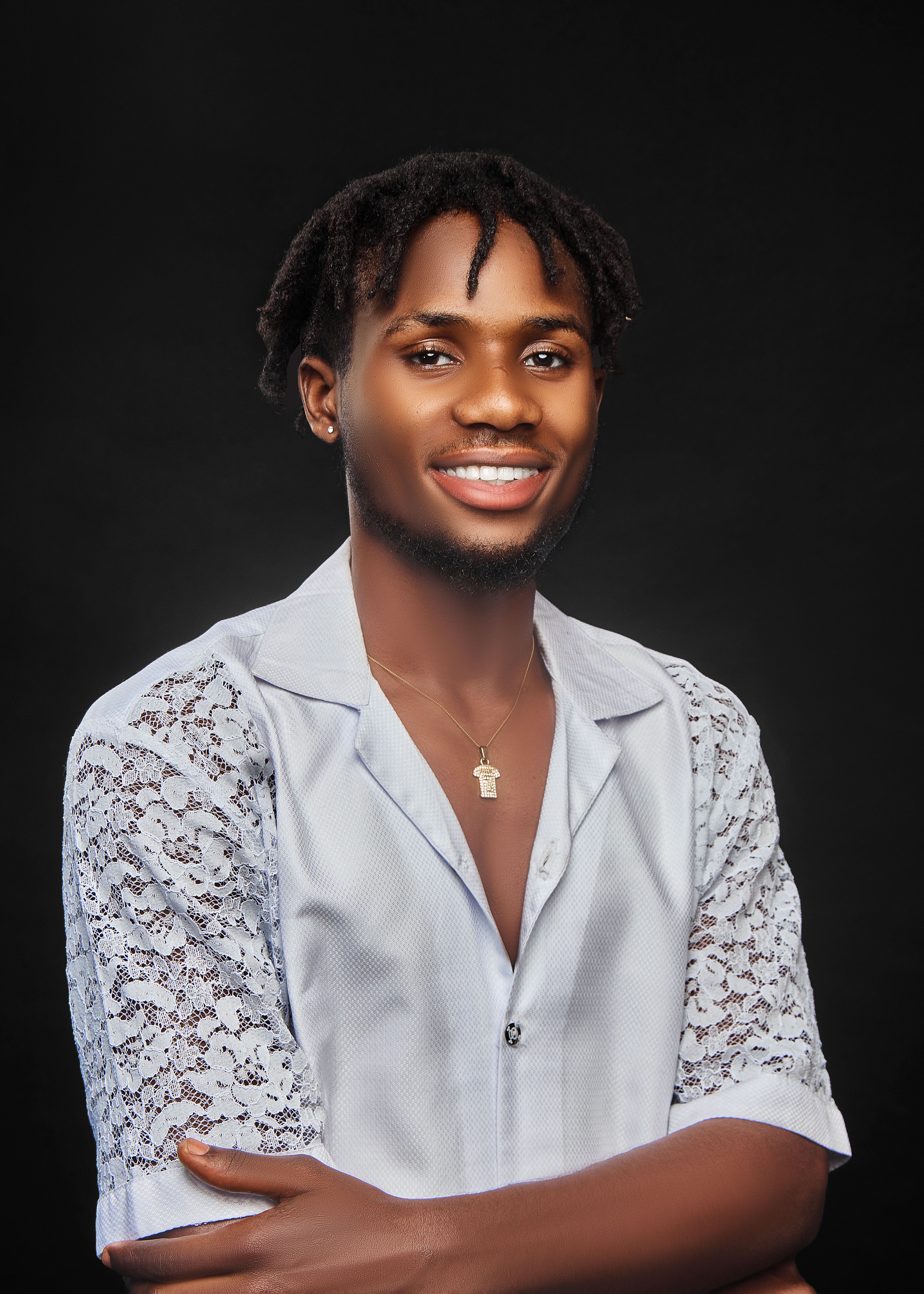 Portrait of a smiling young man wearing a lace shirt against a dark background.