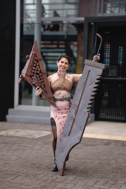 A cosplayer holding two large swords at an outdoor anime event in San José, Costa Rica.
