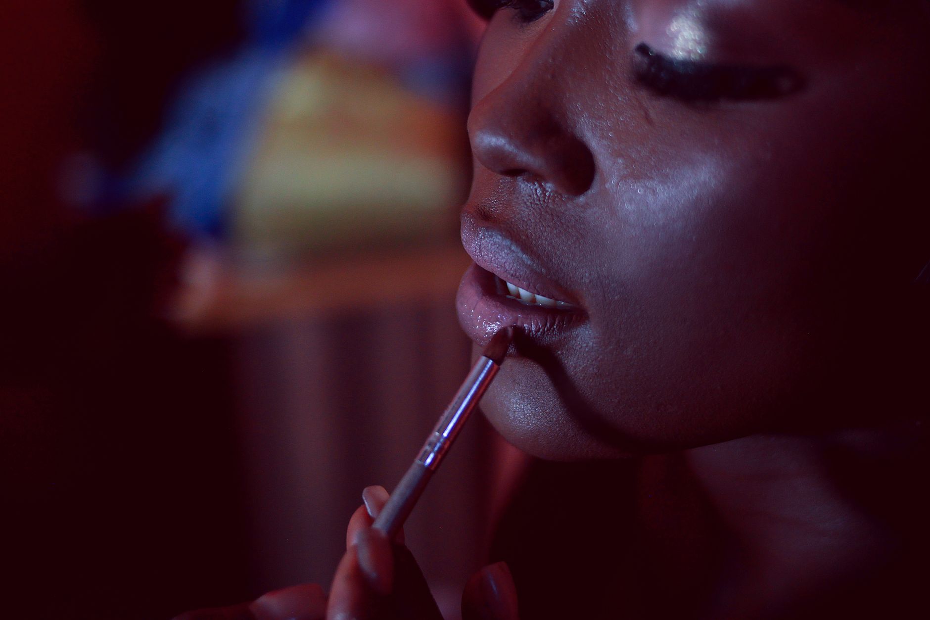 A close-up shot of a woman applying lipstick, highlighting beauty and cosmetics in dim lighting.