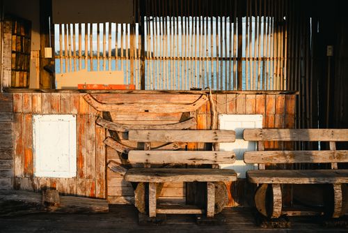 Free Sunlit rustic fishing hut with wooden benches and bamboo fencing, capturing coastal charm at sunset. Stock Photo