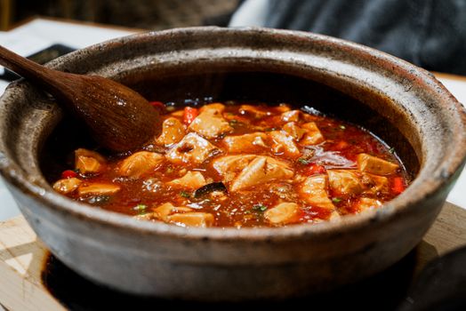 Close-up of a flavorful tofu stew simmering in a rustic pot with a wooden spoon.