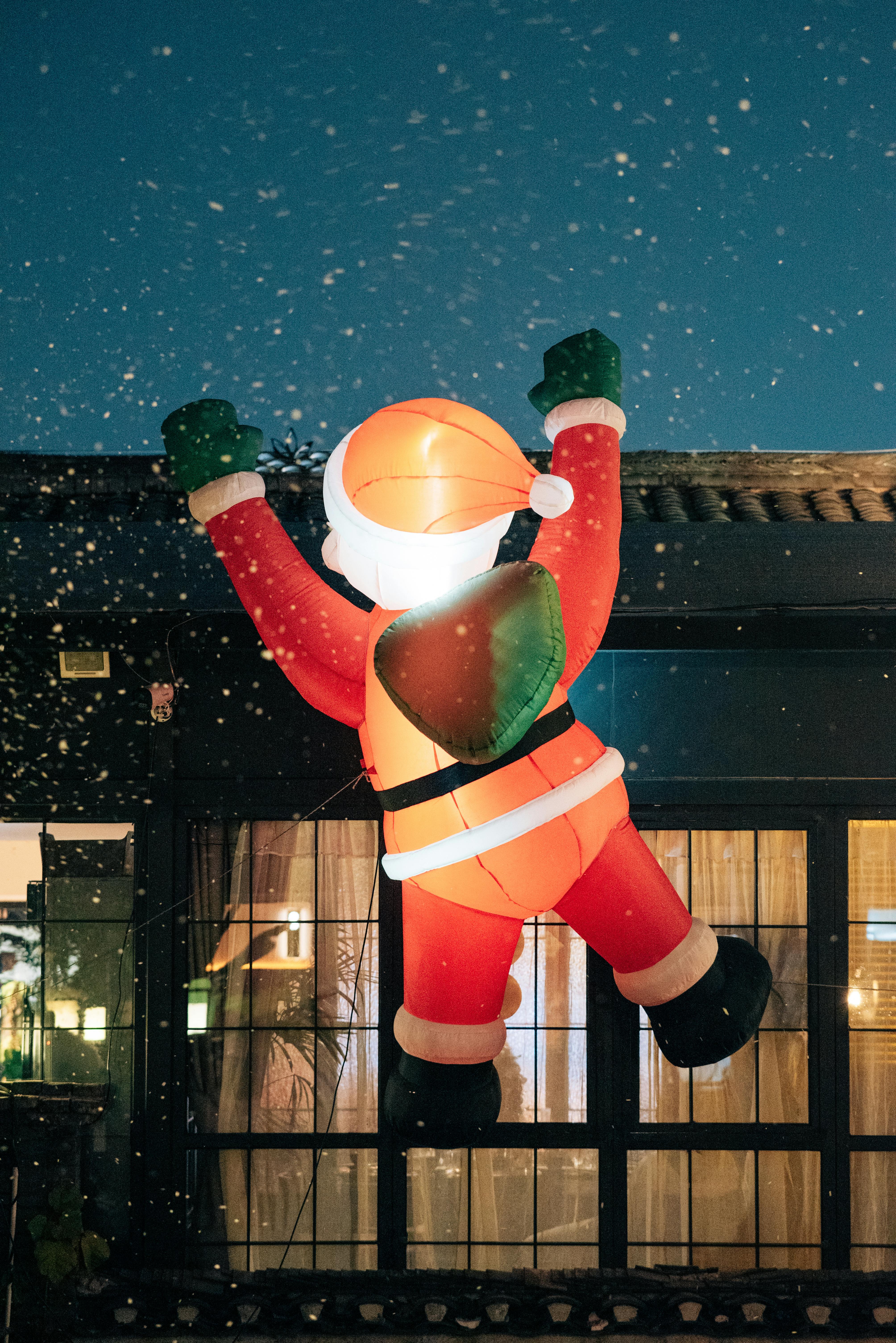 Large inflatable Santa Claus decoration outside during a snowy night. Perfect for holiday themes.