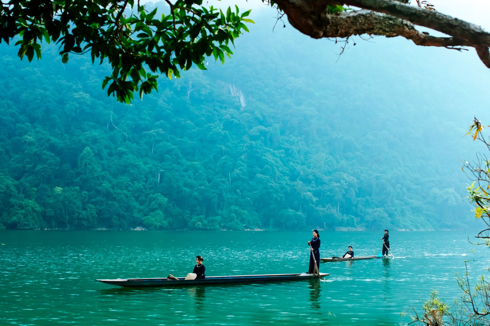 Serene river with three people in wooden boats, surrounded by lush greenery. Tranquil and picturesque.