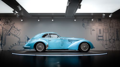 Free A beautifully restored vintage car showcased in a museum setting with a modern backdrop. Stock Photo