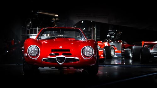 Free Iconic red Alfa Romeo sports car displayed in a dimly lit museum setting. Stock Photo