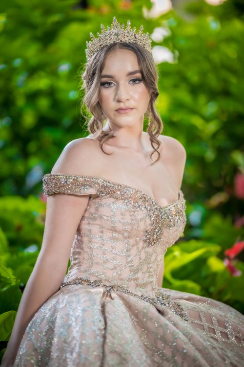 Free A woman in a bejeweled gown poses gracefully outdoors among lush greenery. Stock Photo