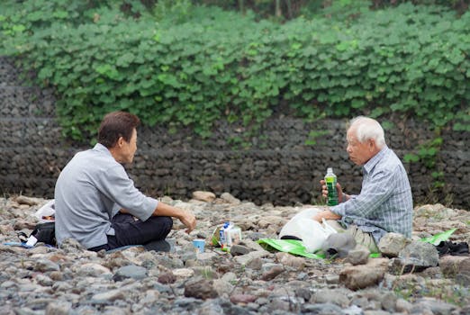 Two elderly men enjoying a relaxed picnic on a rocky terrain in Saitama, Japan.