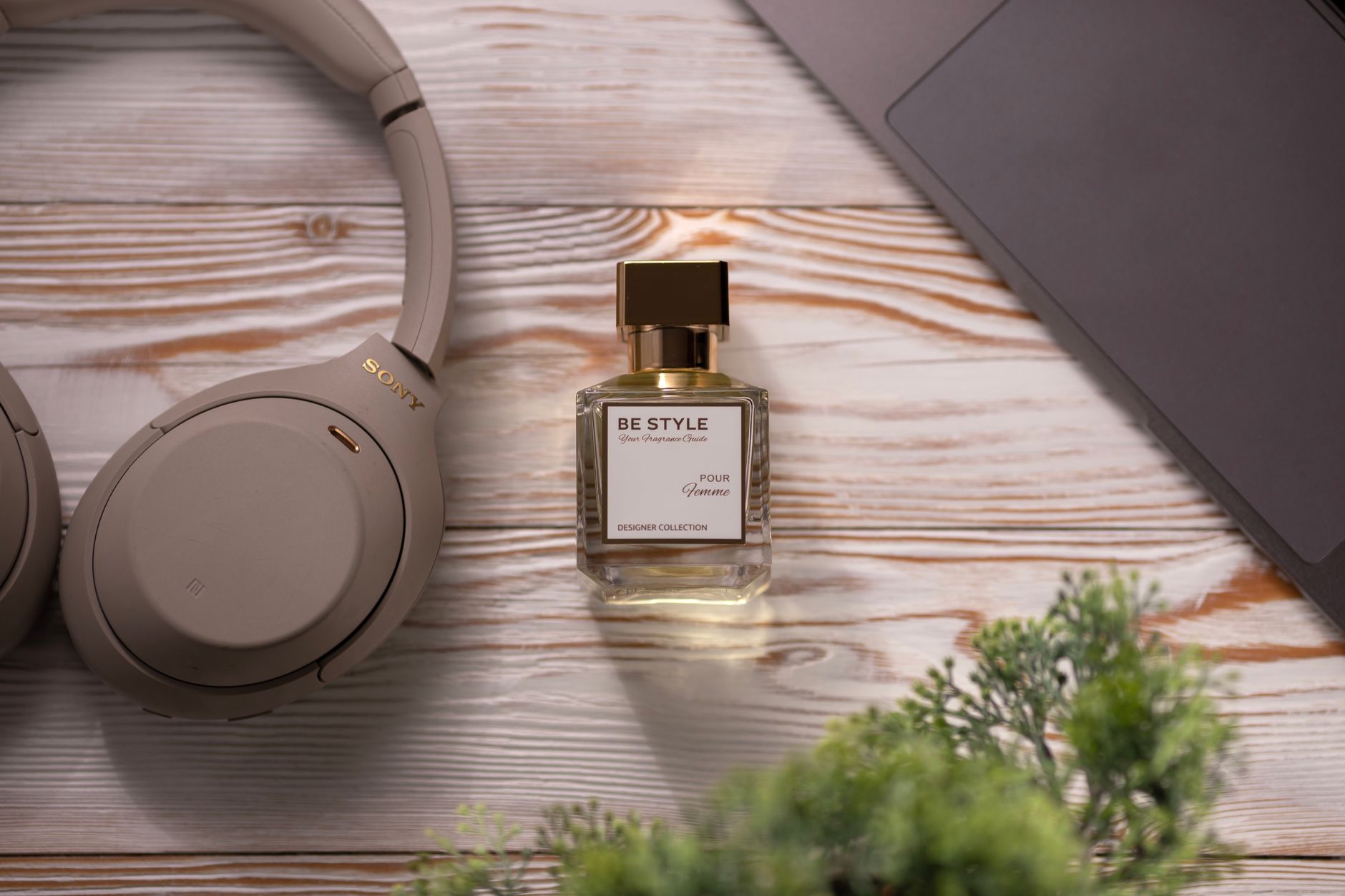 A stylish perfume bottle beside headphones and laptop on a wooden surface.