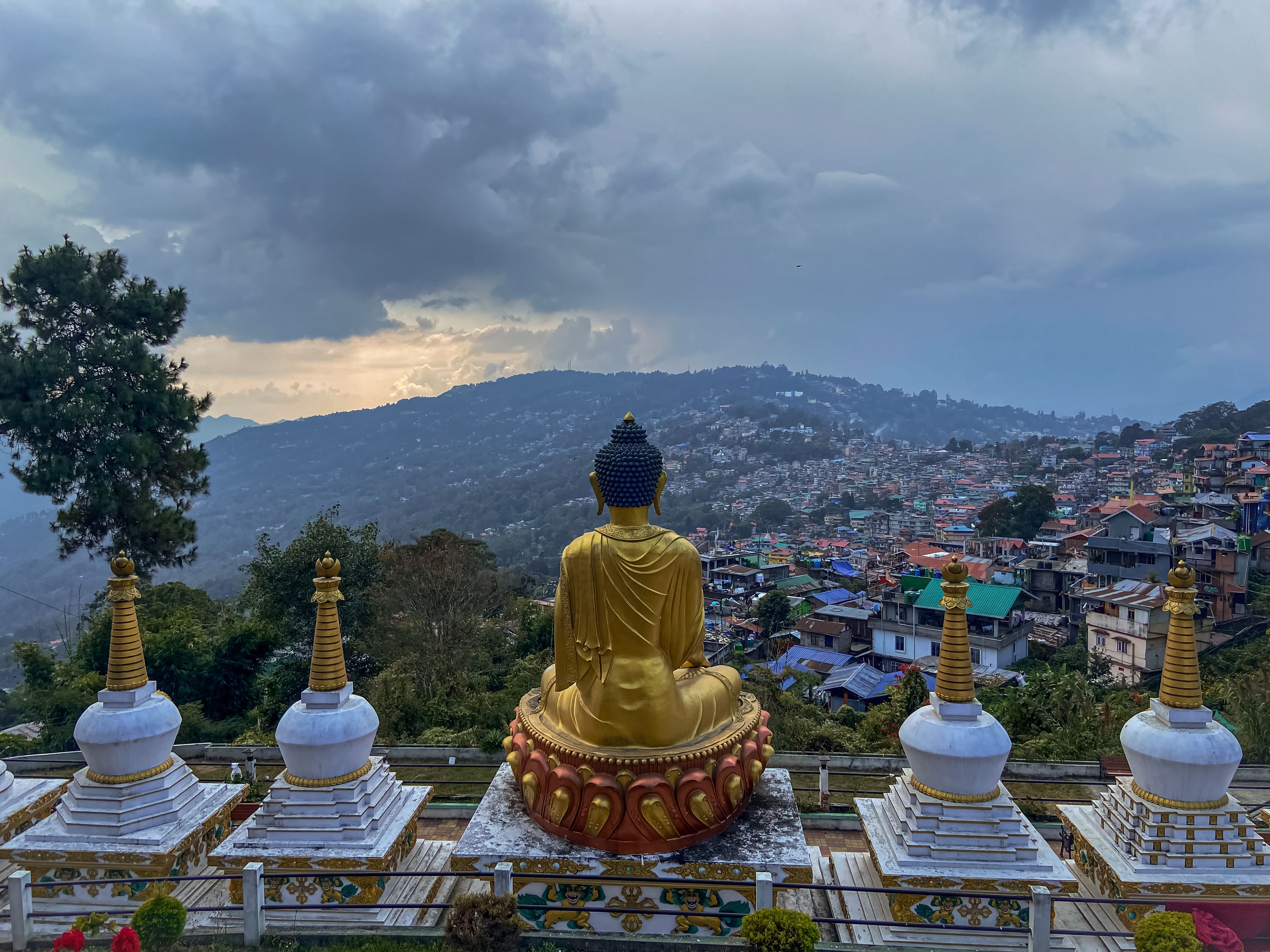 Un Buda dorado y estupas blancas en una colina de Kalimpong que mira a la ciudad al anochecer, bajo nubes de invierno