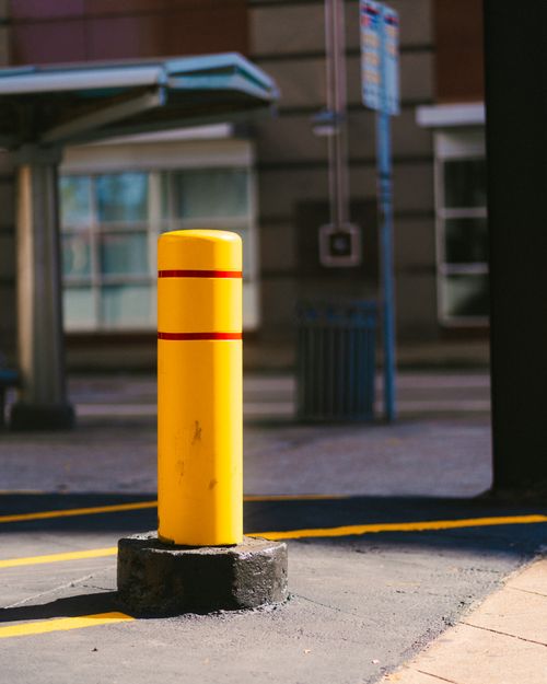 Free A vibrant yellow traffic bollard in a city street with modern architecture. Stock Photo