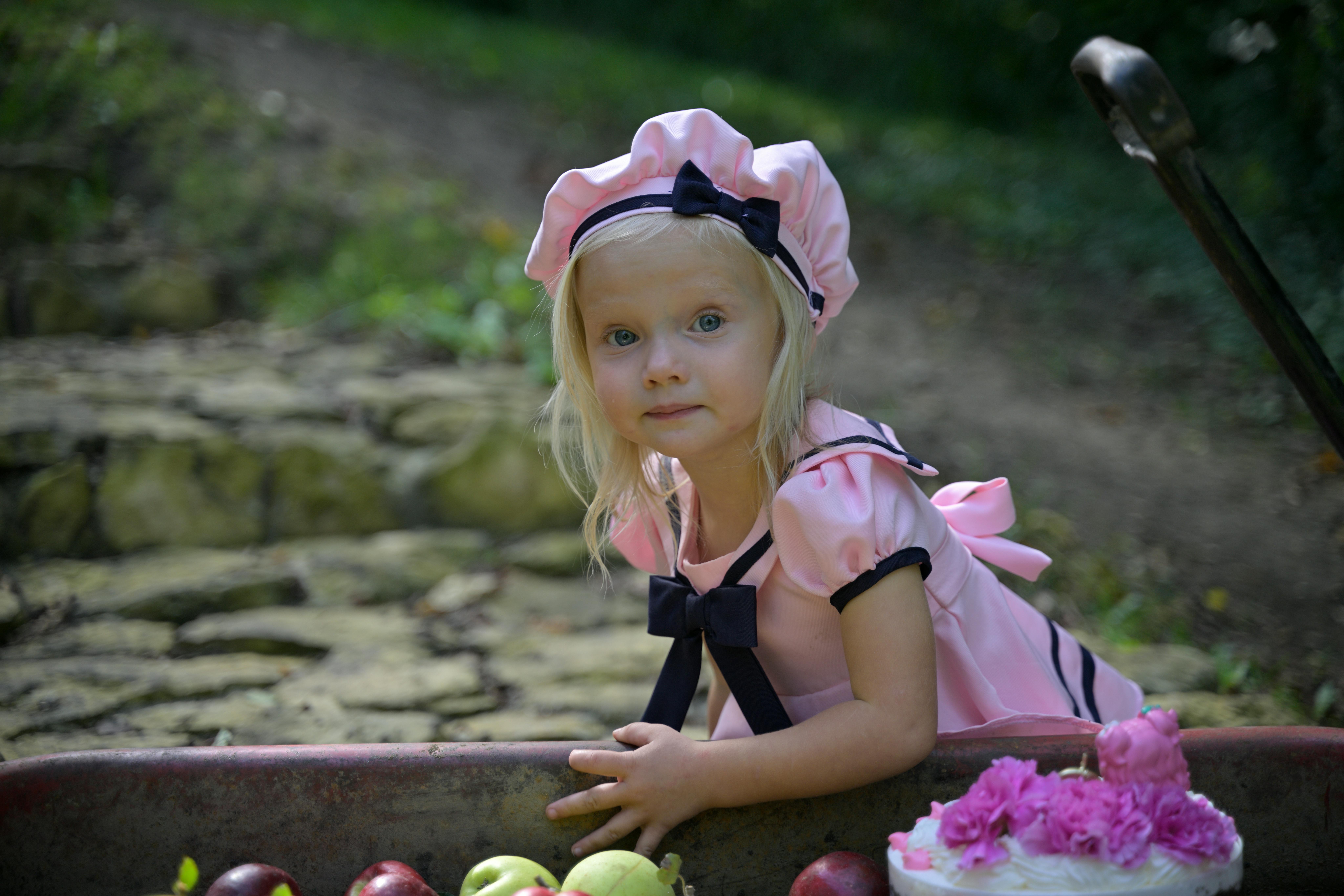 gratis Een jong meisje in een roze jurk en muts poseert buiten met appels en bloemen. Stockfoto