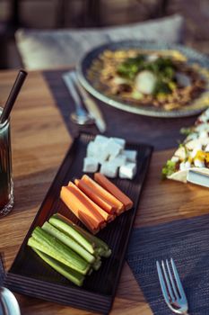 A vibrant assortment of vegetables and cheese on a wooden table set for dining.