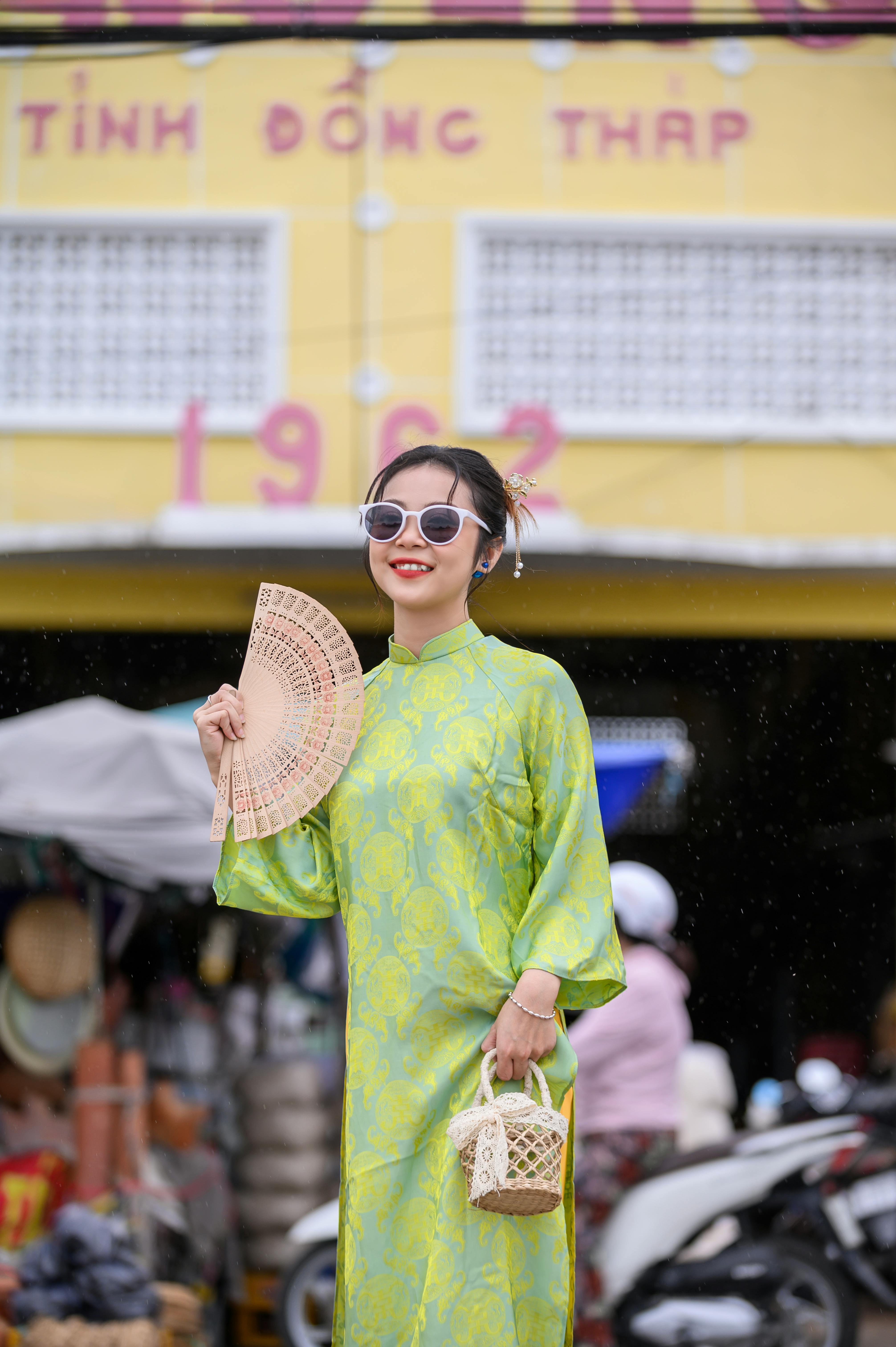 Smiling woman in traditional dress holding a fan at a market, evoking cultural charm.