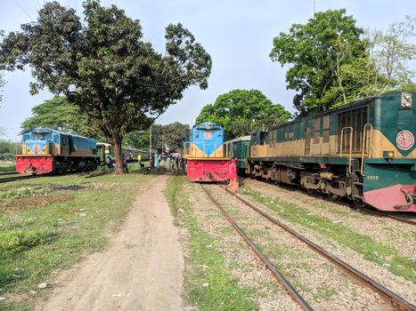 A lively railway scene in Bangladesh with trains, people, and lush greenery.