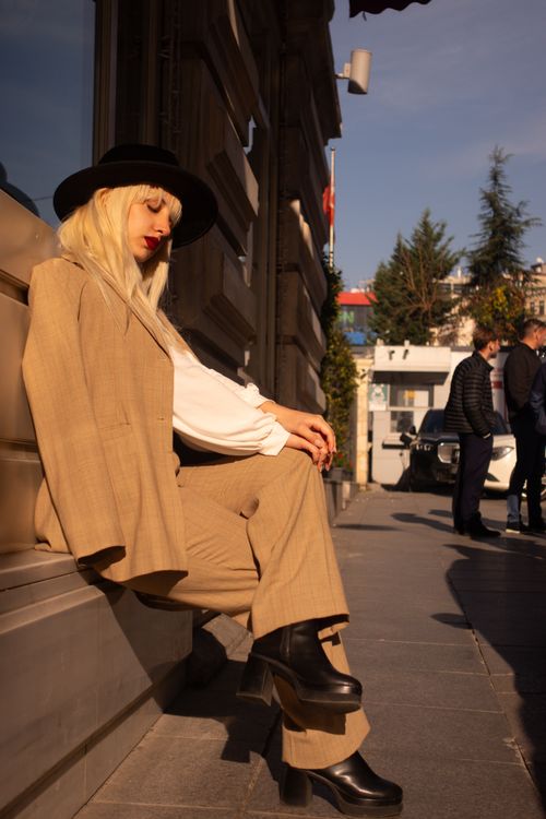 Free Fashionable woman in a suit and hat sits on a street in İstanbul under sunlight, exuding 80s style. Stock Photo