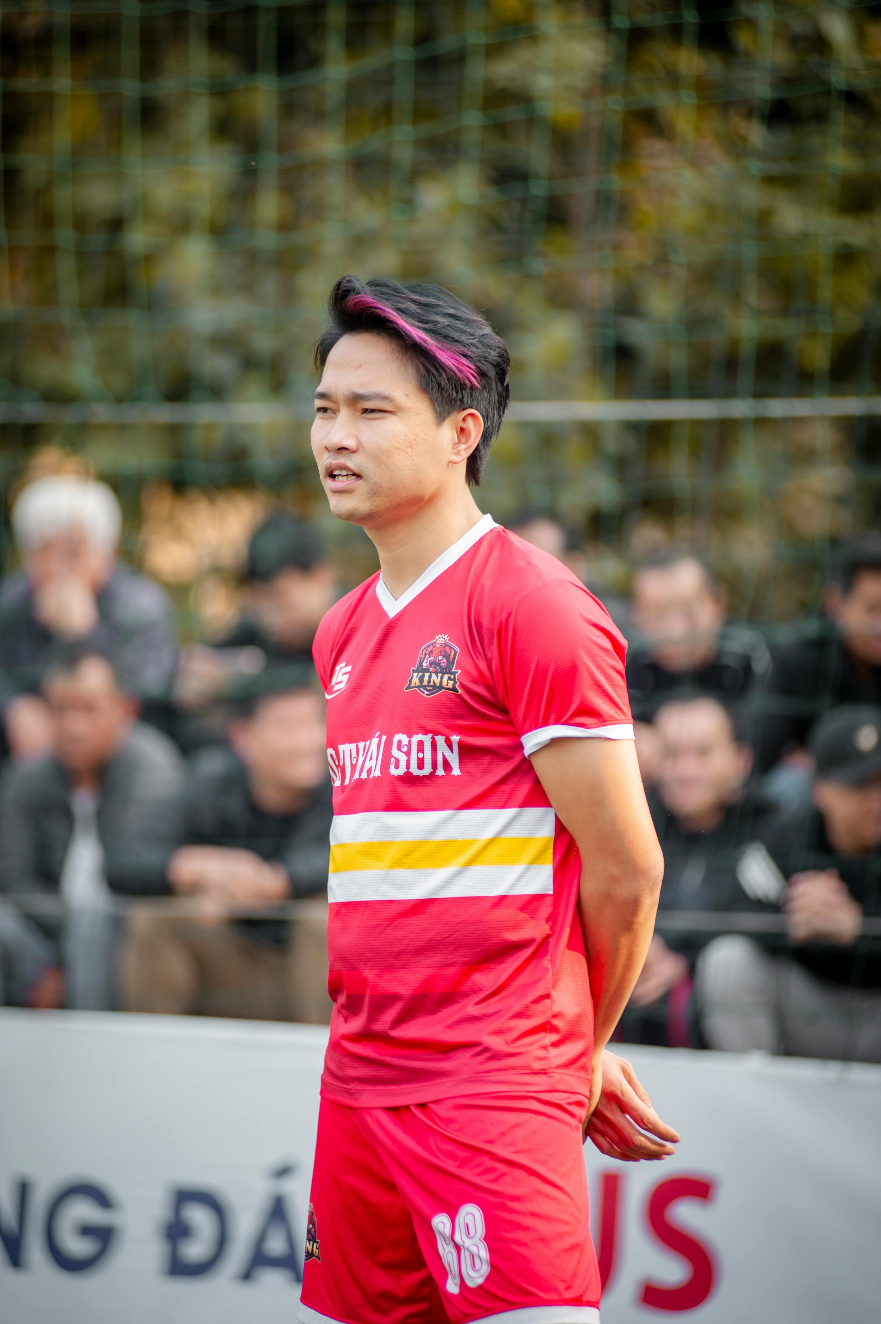 Focused soccer player in vibrant red uniform during a local match in Hà Nội, Việt Nam.