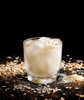 A refreshing creamy beverage served in a glass with ice, surrounded by oats and sugar.