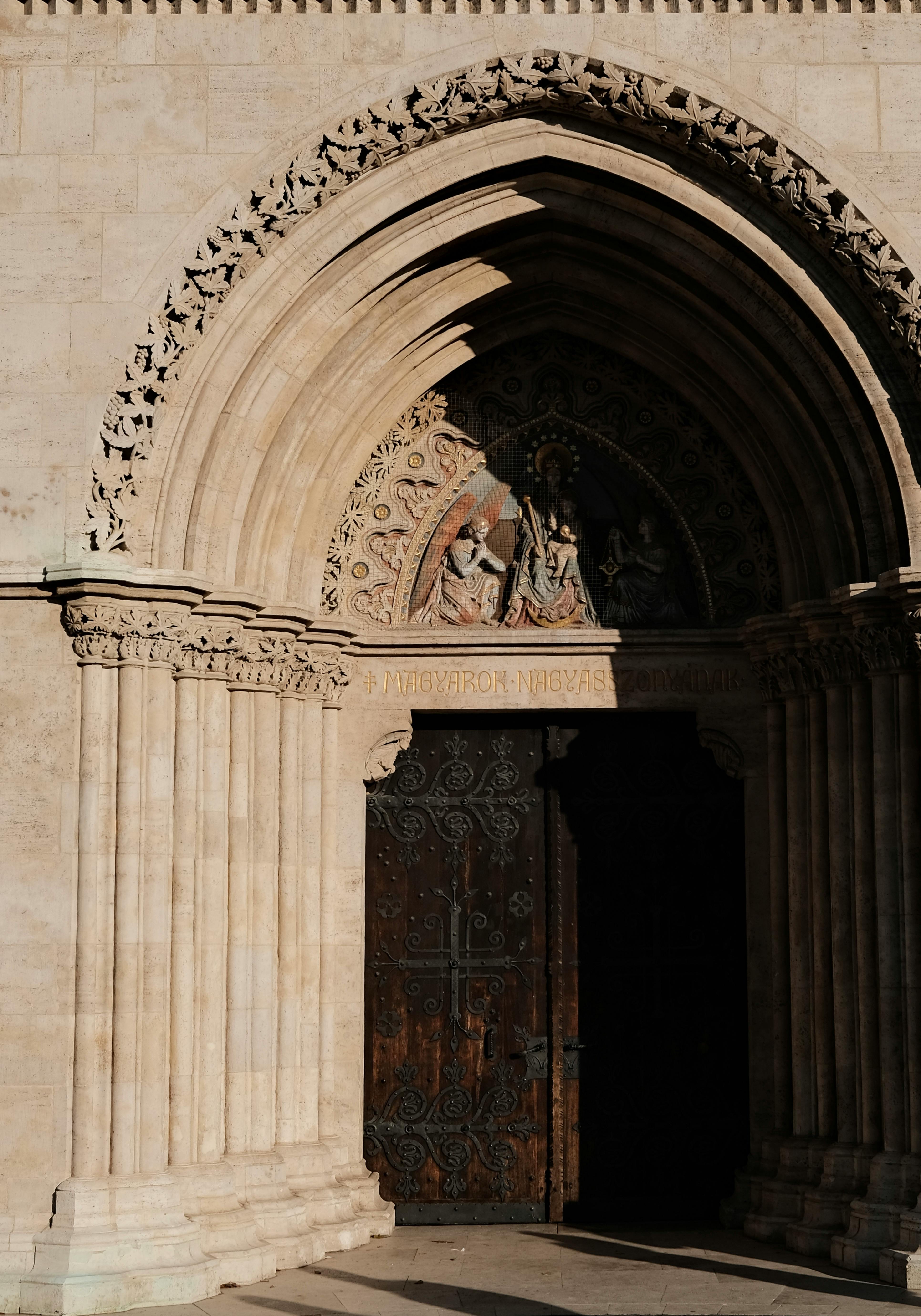 Sunlight illuminates a detailed Gothic church door and archway with intricate sculptures.