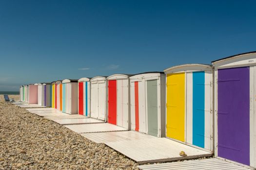 Vibrant beach huts on a pebble beach in Le Havre, Normandy, France, on a sunny day.