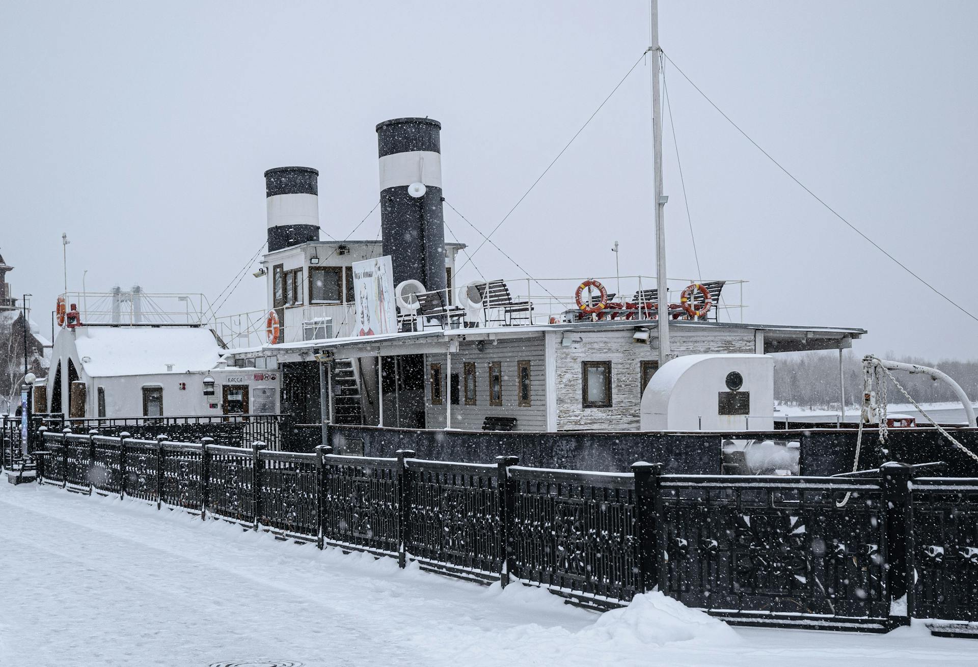 A vintage steamboat sits docked in a snowy port, highlighting winter's serene beauty.