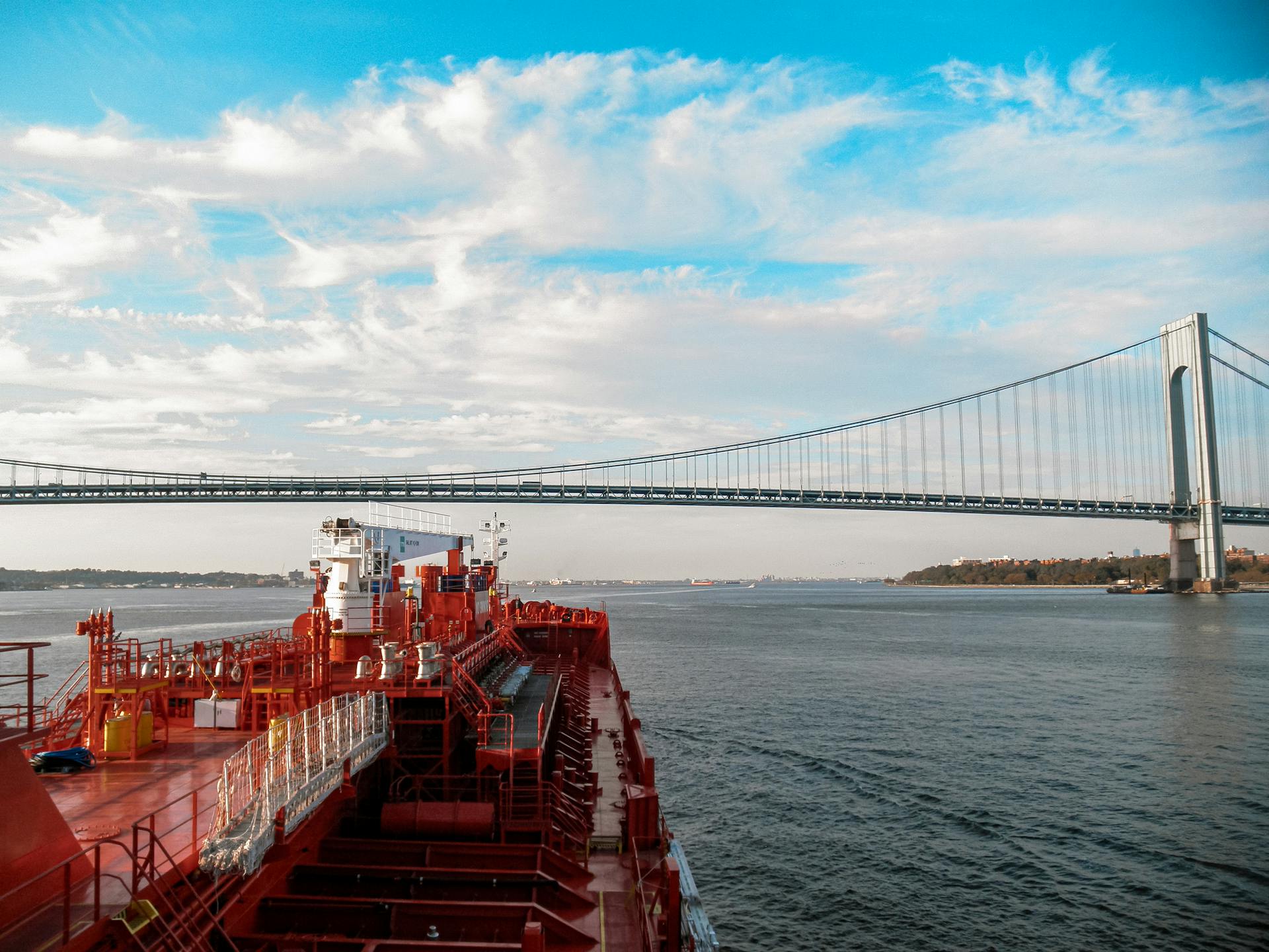 Tanker ship navigating under the iconic Verrazzano-Narrows Bridge on a clear day.